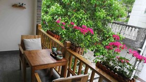 Un balcón de madera con una mesa y sillas, rodeado de plantas y flores en macetas.