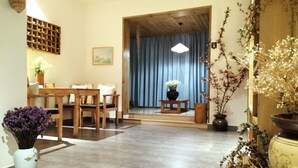 Una habitación tradicional japonesa con suelo de tatami, una mesa baja con cojines, una estantería de madera con objetos decorativos y vistas a un fondo de cortina azul a través de una pantalla shoji.