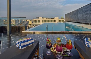 Piscina en la azotea con vistas a la ciudad, sillas de descanso y una mesa con bebidas y aperitivos.