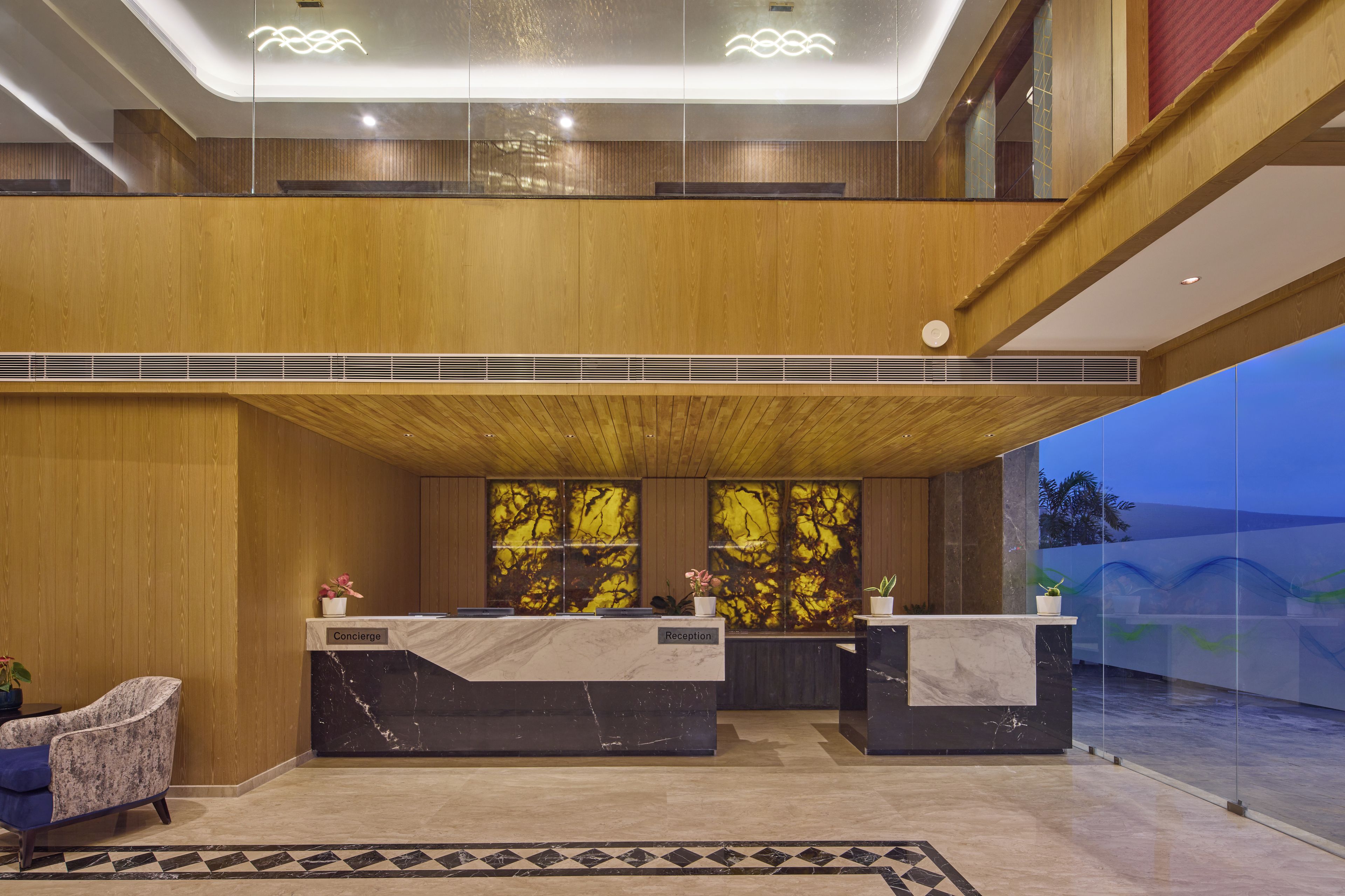 A hotel reception area with a modern design, featuring a wooden ceiling, marble reception desks, and a glass partition.