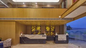 A hotel reception area with a modern design, featuring a wooden ceiling, marble reception desks, and a glass partition.