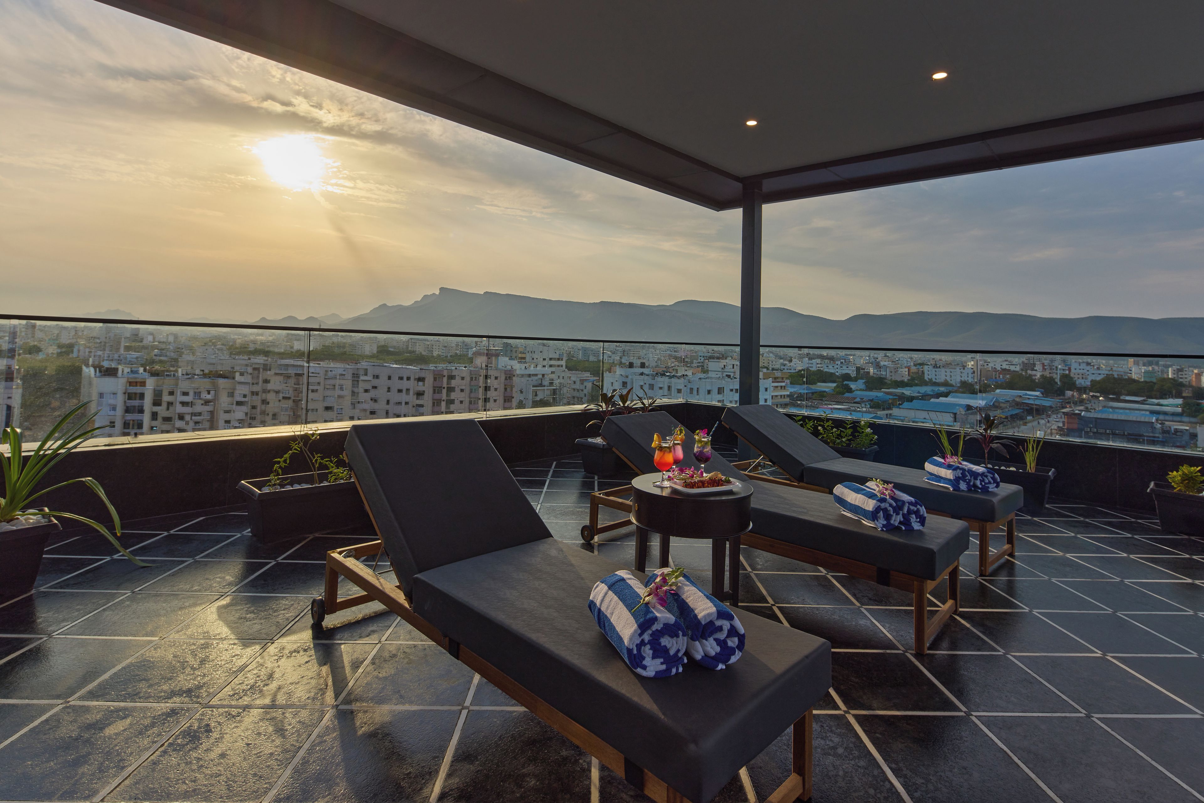 Eine Dachterrasse mit Liegestühlen, einem Tisch mit Getränken und Blick auf die Stadt.
