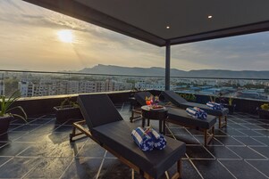 Una terraza en la azotea con sillones, una mesa con bebidas y vistas panorámicas de la ciudad.
