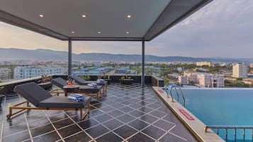 A rooftop terrace with lounge chairs, a swimming pool, and a city view.