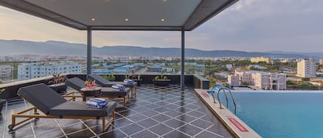 Terraço no telhado com cadeiras de lounge, piscina e vista para a cidade.
