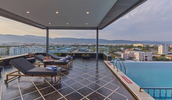 A rooftop terrace with lounge chairs, a swimming pool, and a city view.