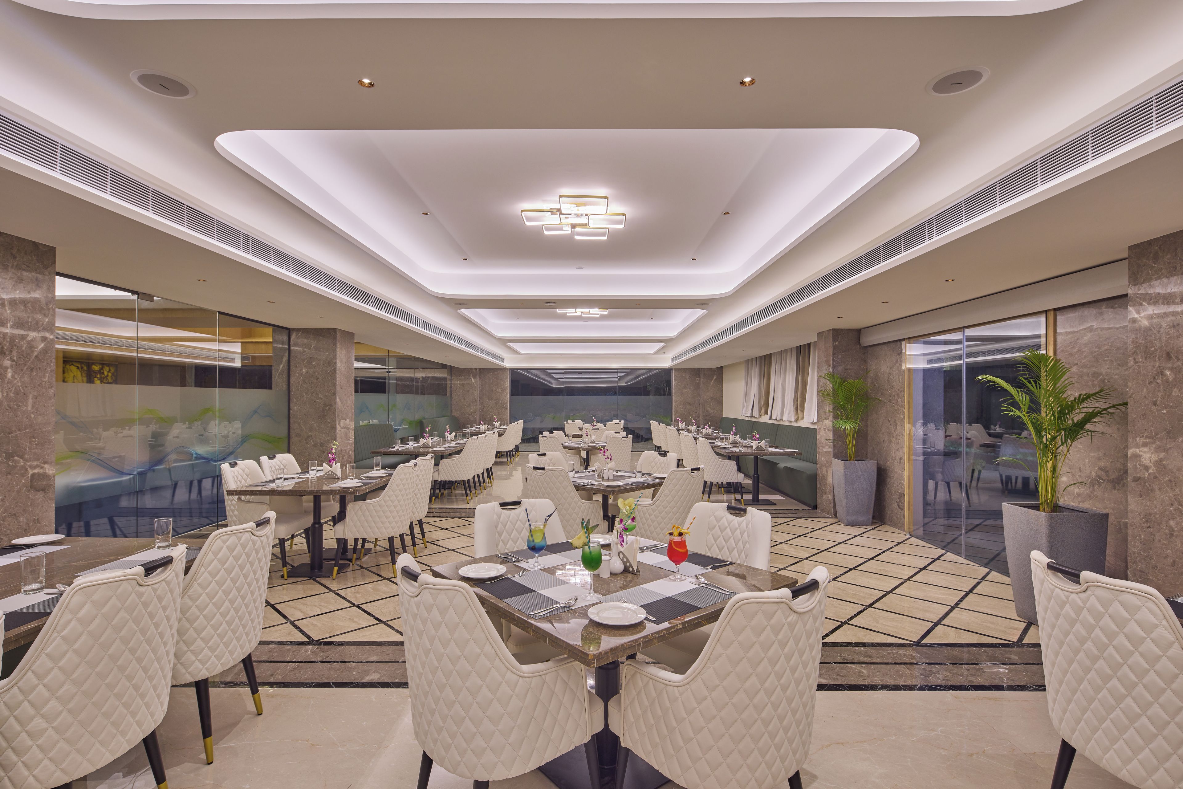 A spacious dining area with multiple tables and chairs, a modern ceiling design, and large windows.
