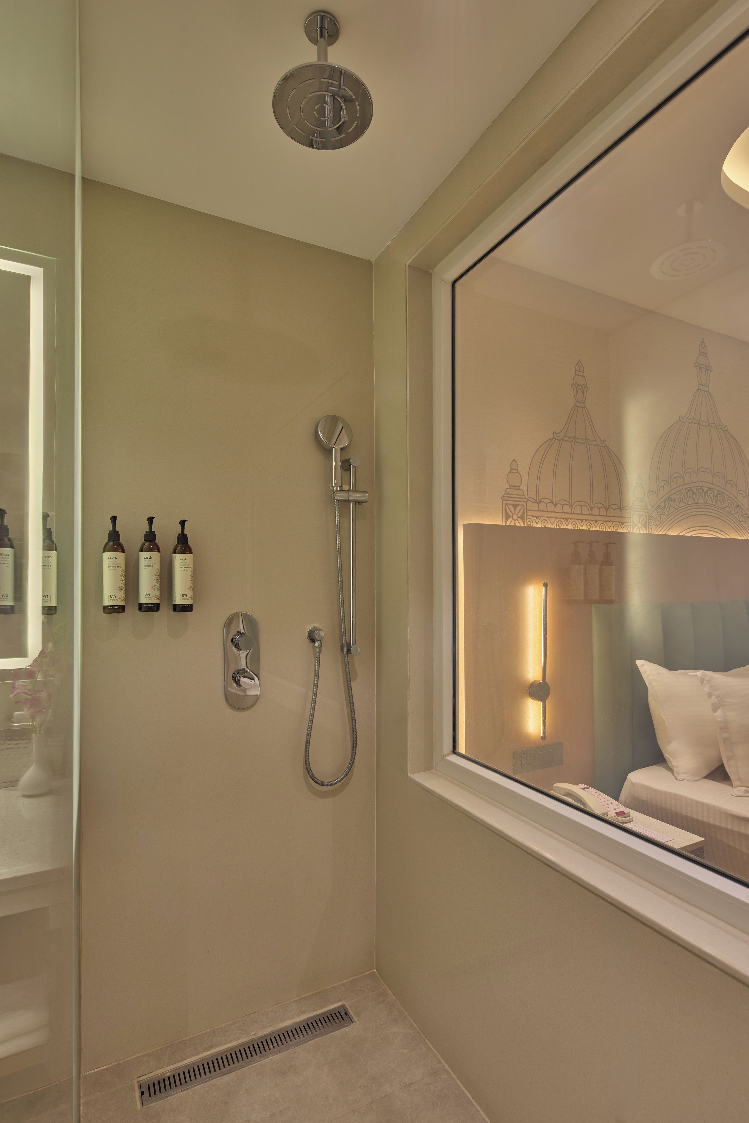 Une salle de bain avec une douche, une fenêtre donnant sur un immeuble et des articles de toilette fixés au mur.