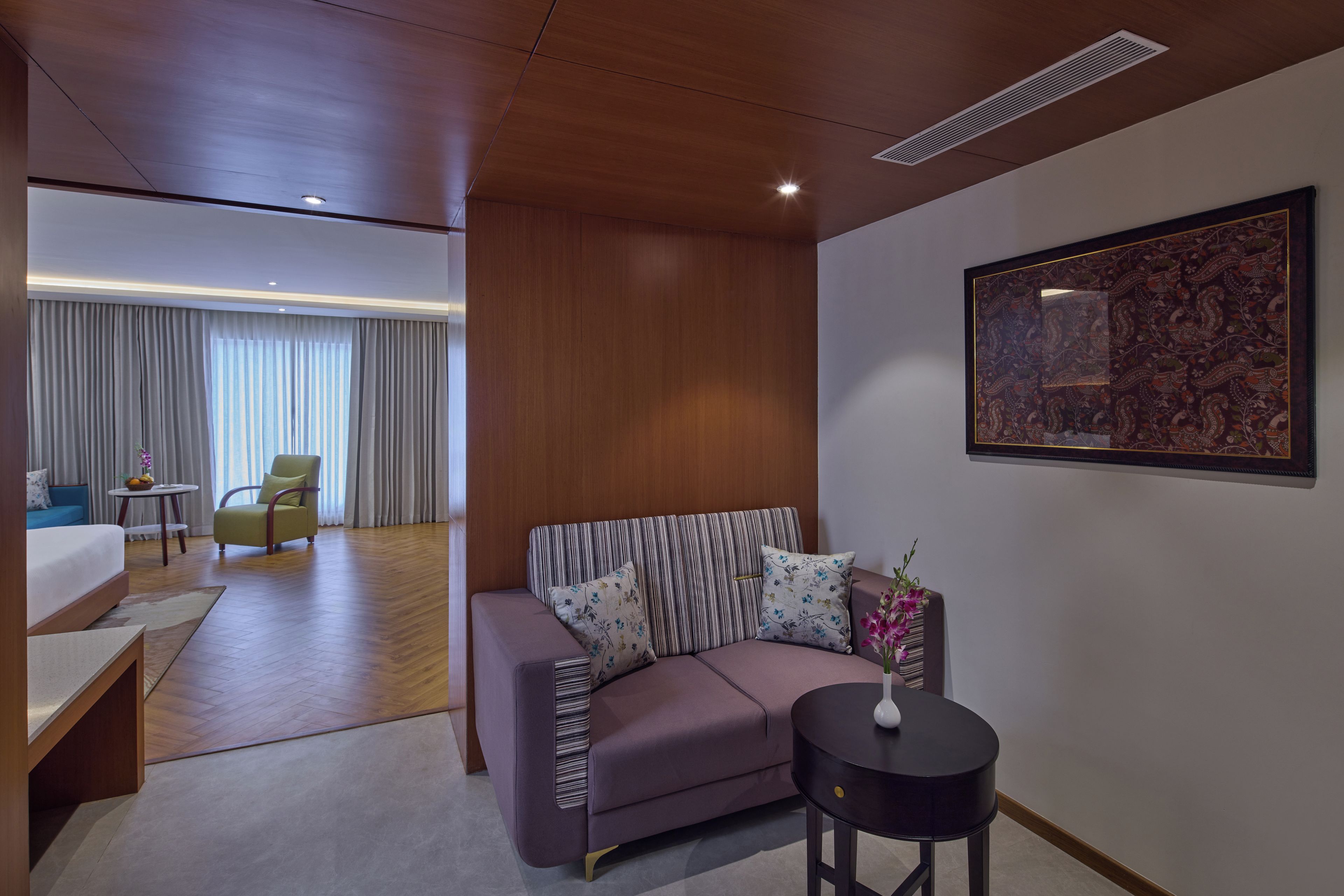 A modern hotel room with a sofa, a small table, a decorative vase, and a large abstract painting on the wall.