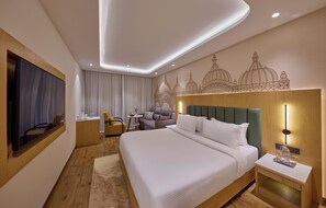 A hotel room with a large bed, a TV, a desk, a chair, and a decorative wall mural.