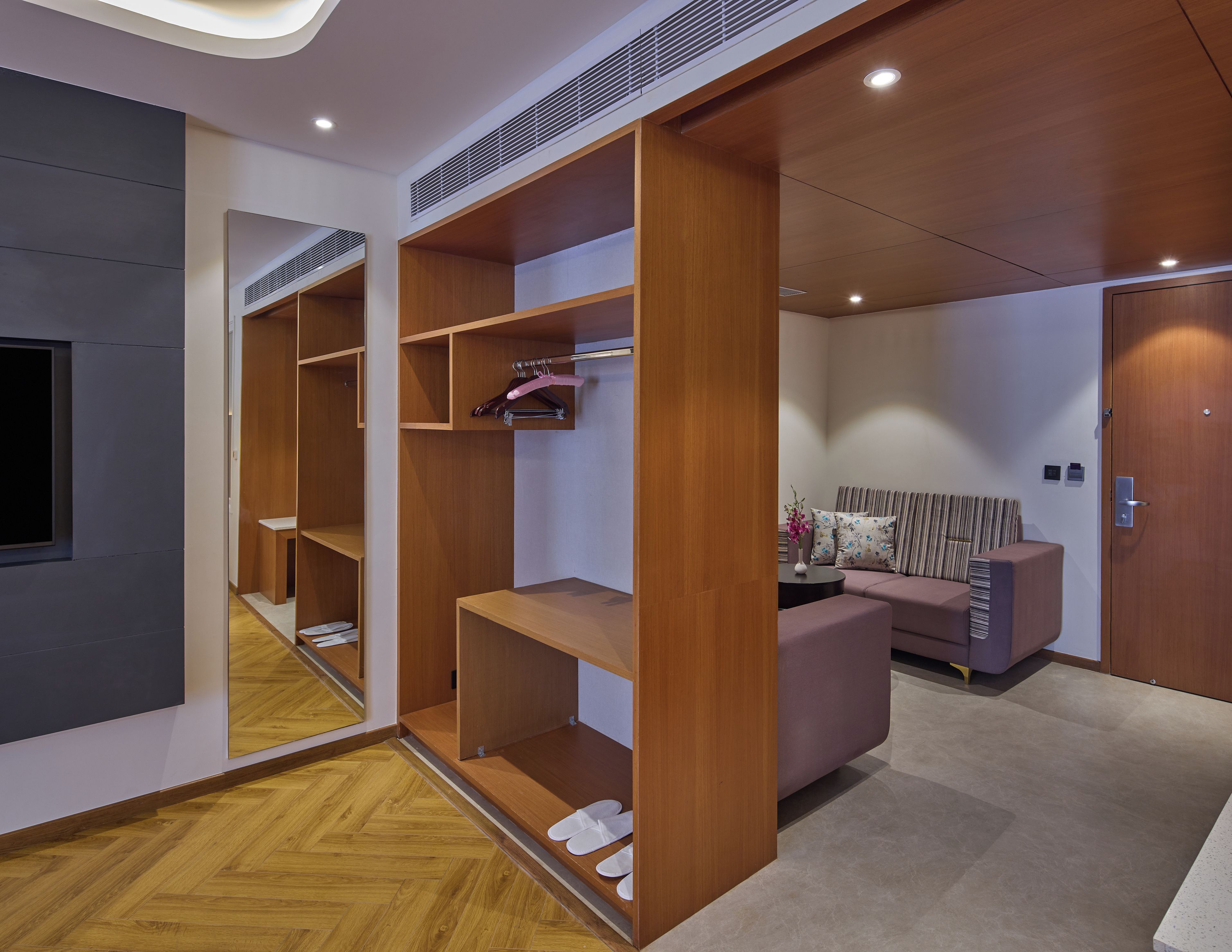 Un intérieur moderne avec une armoire en bois, un coin salon comprenant un canapé et des fauteuils, et un miroir qui reflète l’espace.