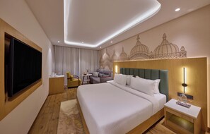 A modern hotel room with a large bed, a flat-screen TV, a desk, a chair, and a decorative wall mural.