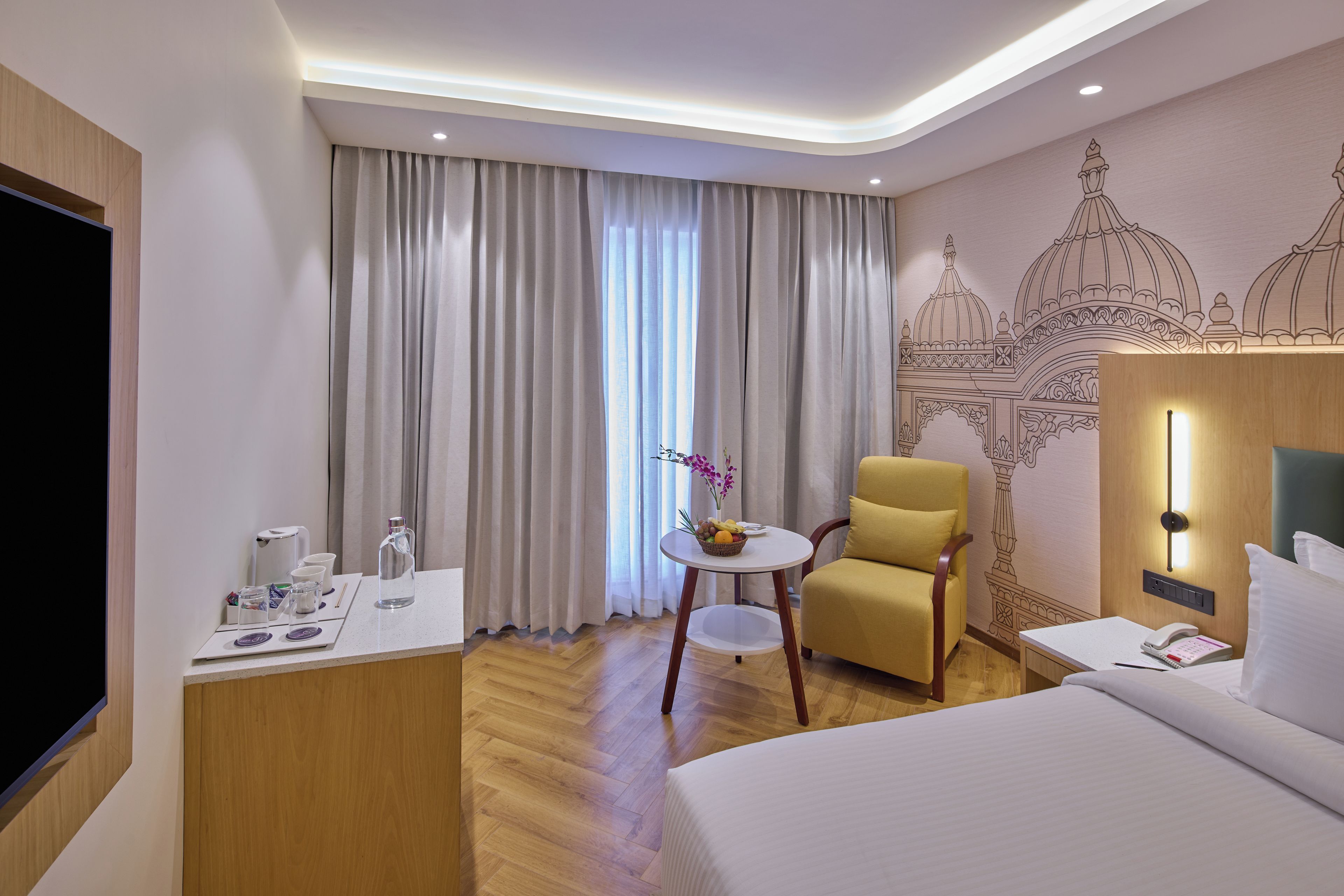 Une chambre d’hôtel avec un lit, un bureau avec un téléphone, une chaise et une table sur laquelle se trouve un panier de fruits.