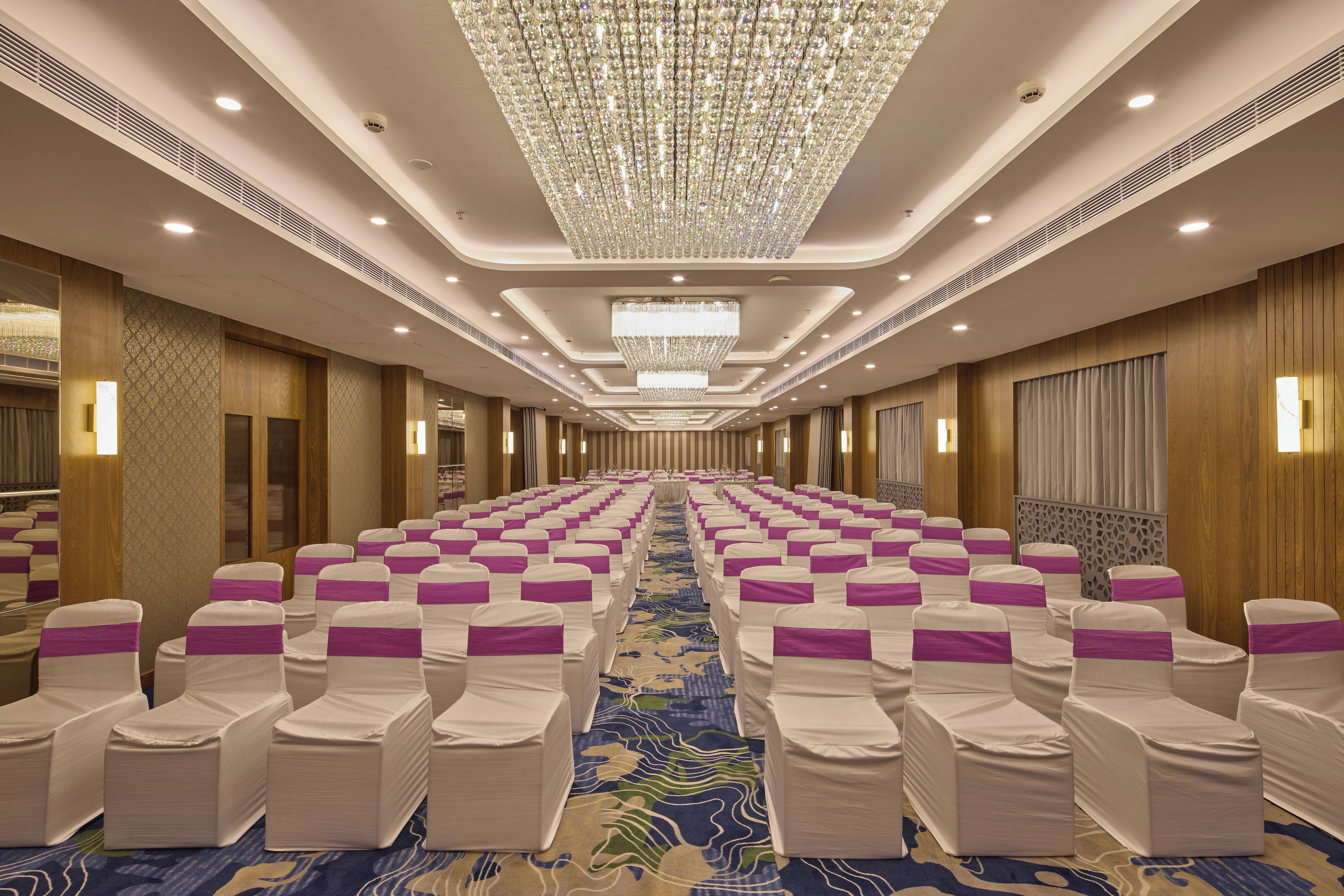 Un salón de conferencias de hotel con hileras de sillas, una alfombra estampada y una gran araña.