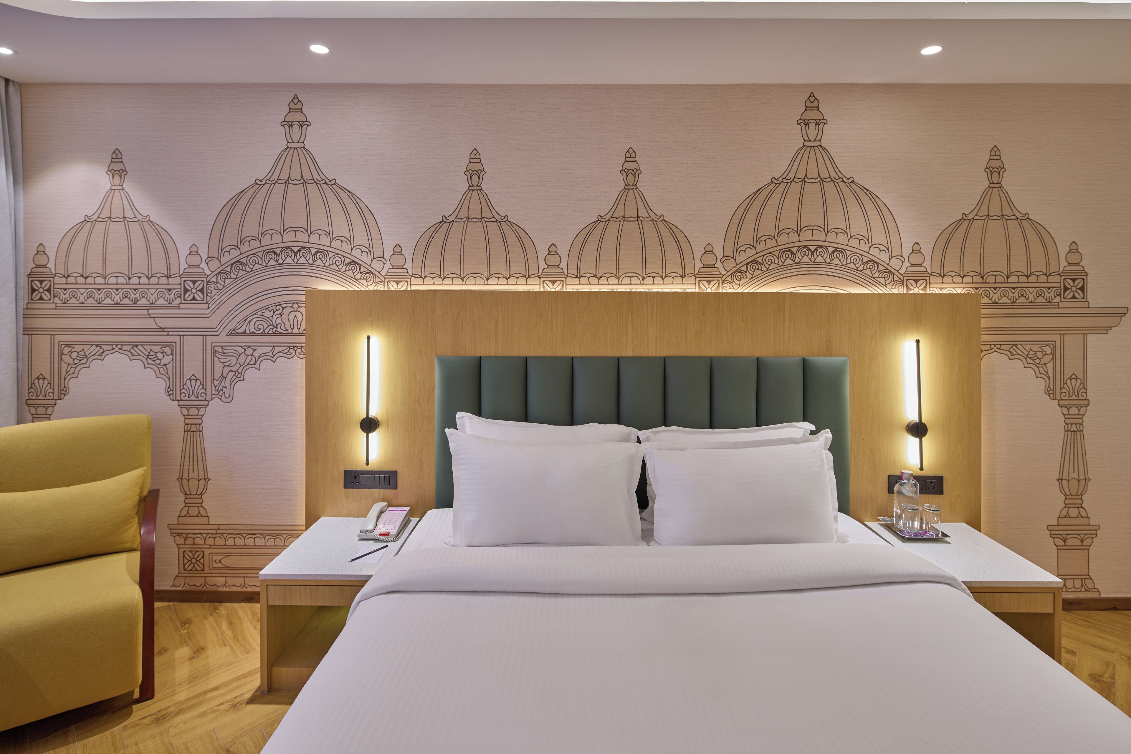 A hotel room with a large bed, two bedside tables, a nightstand, a chair, and a wall with a decorative pattern.