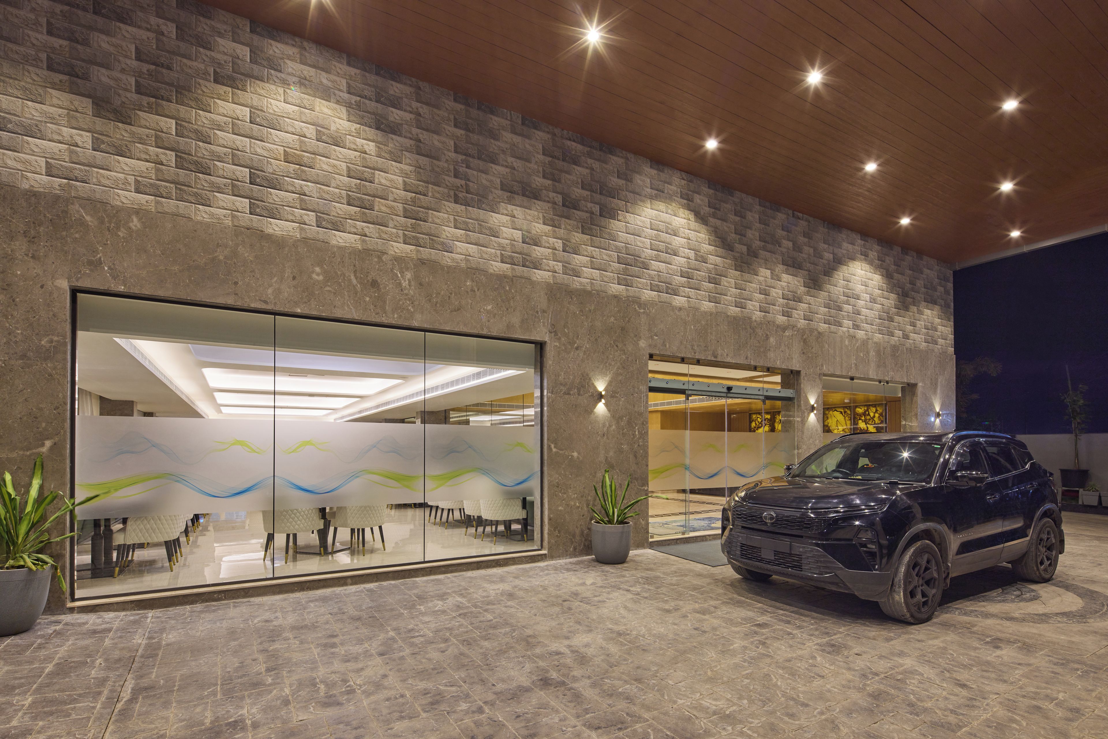 A modern building with a brick facade, large glass doors, and a parked SUV.