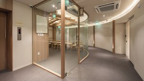 Ein modernes Interieur mit Glastrennwand, einer digitalen Aufzugsanzeige und einem Konferenzraum mit Tischen und Stühlen.