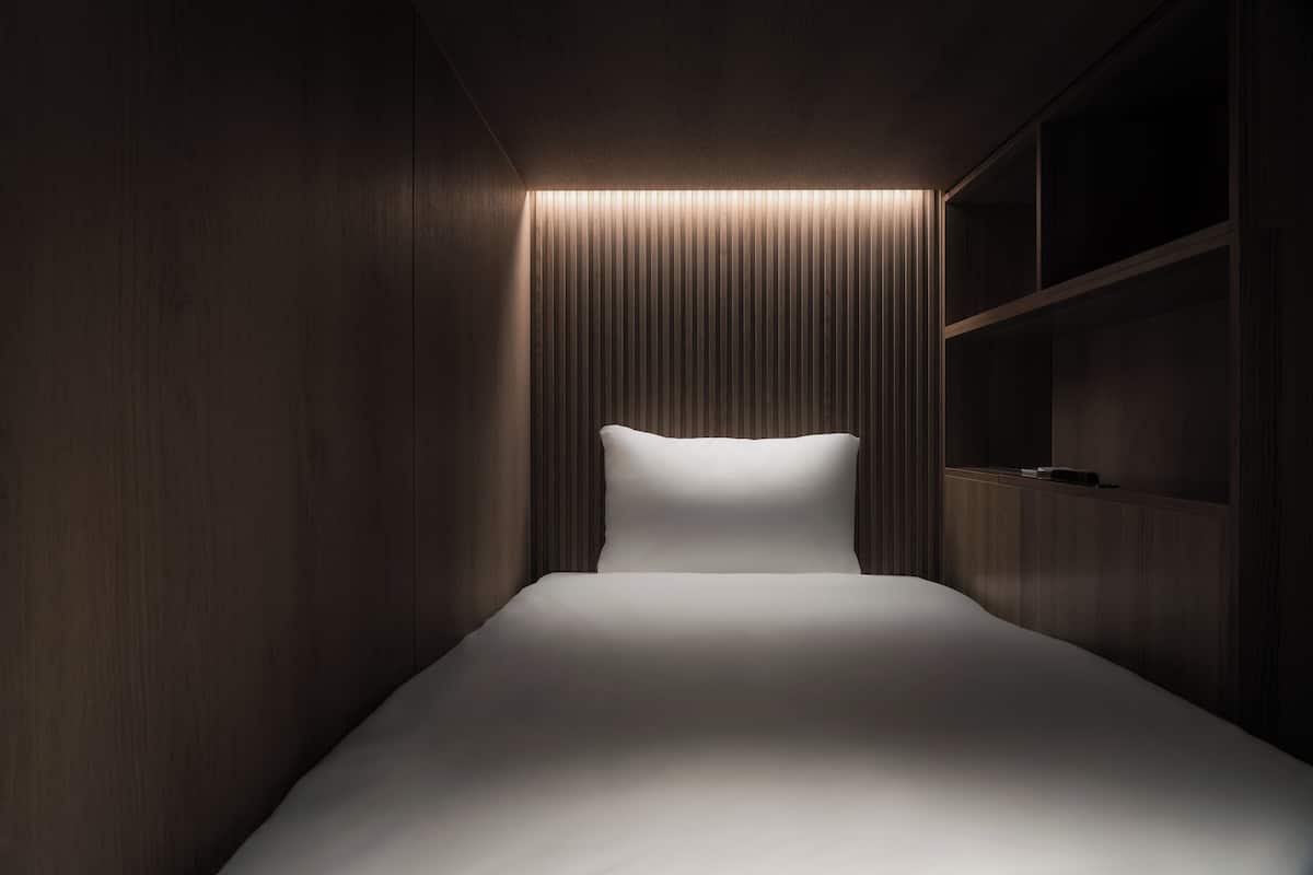 A modern, dimly lit room with a single bed, wooden paneling, and built-in shelving.