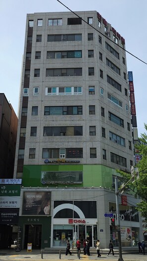A multi-story building with commercial spaces on the ground floor, including a visible entrance to a store with a green awning. - KANSO STAY (Seoul)