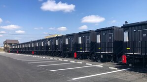 A row of black shipping containers with white number labels, parked in a parking lot with white parking lines. - HOTEL R9 The Yard Hanazonointer (Fukaya)