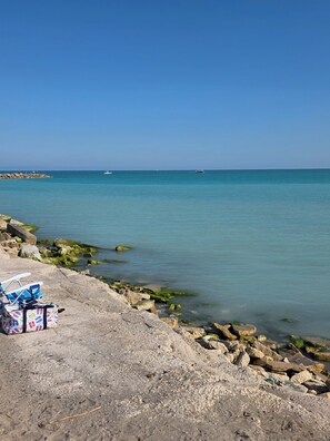 Eine felsige Küstenlinie mit klarem, blauem Wasser, einigen Booten und einem Liegestuhl.