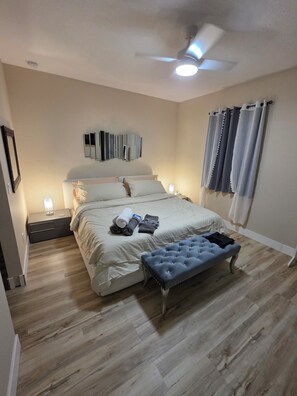 A bedroom with a bed, bedside lamps, a ceiling fan, and a window with curtains. - HOME SWEET HOME (Fort Pierce)