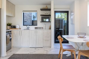 A modern kitchen with a central island, built-in appliances, and a dining area with a table and chairs. - Central Townhouse Near One NZ Stadium & Te Pae (Christchurch)