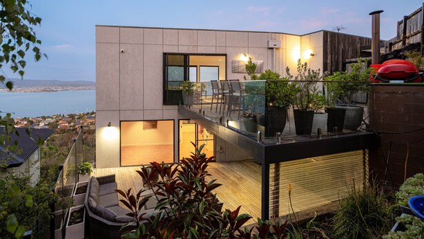 A modern two-story building with a balcony, outdoor seating, and a view of the sea.