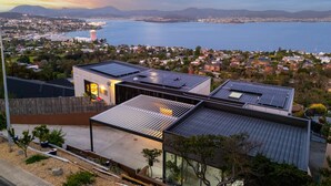 A modern building with solar panels, a view of a coastal cityscape, and a body of water in the background.