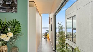 A hallway with a view of a body of water, a potted plant, and a framed picture on the wall.