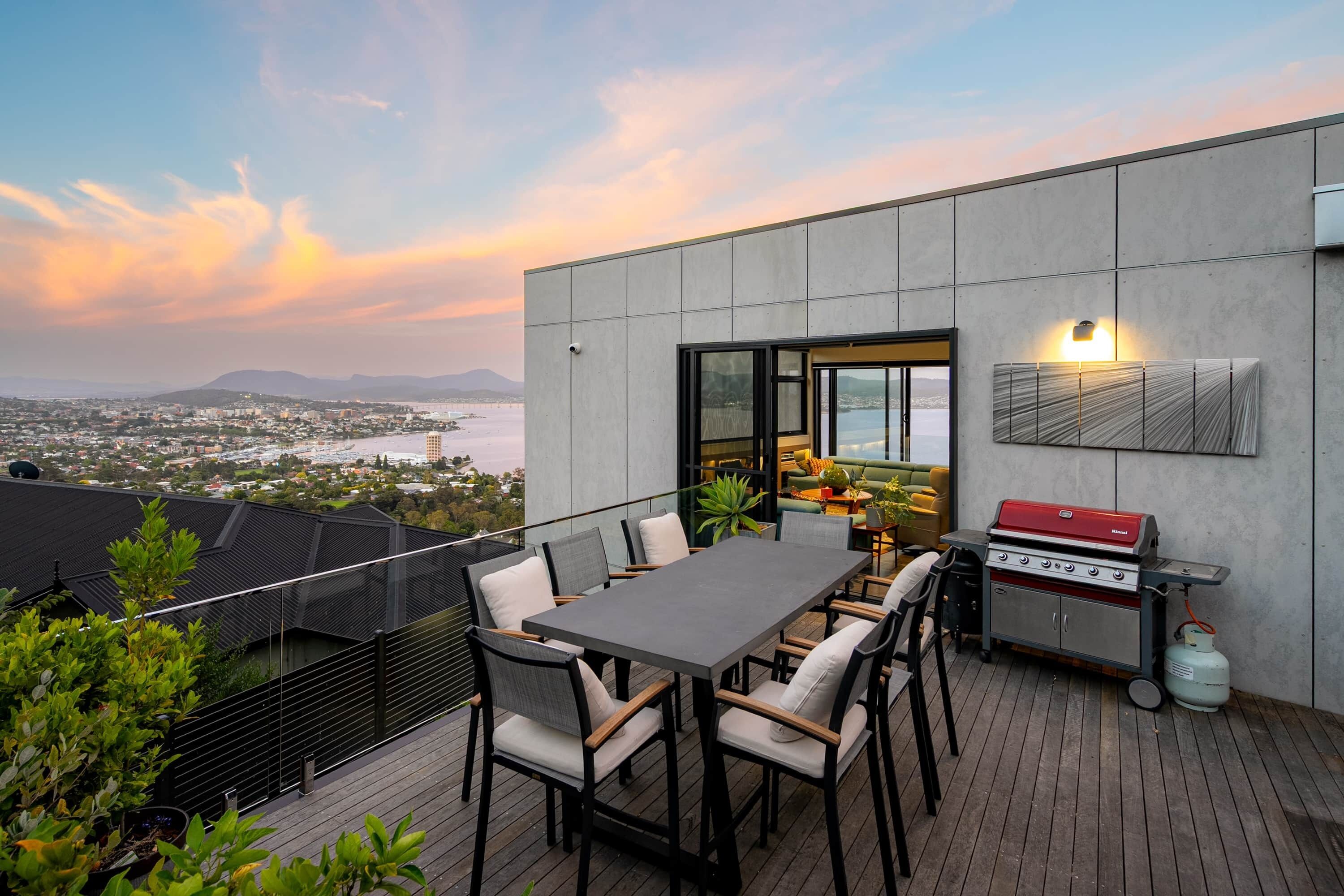 An outdoor patio with a table and chairs, a grill, and a view of the cityscape.