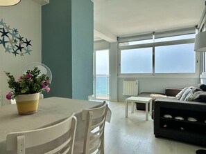 A modern living room with a dining area, large windows, and a view of the sea. - Sicamar Apartment – Seaside Getaway in Platja d’Aro (Platja d'Aro)