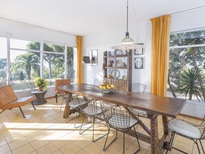 Ein Essbereich mit Holztisch, Drahtstuhlen, einer Topfpflanze und einer Obstschale.