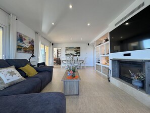 A modern living room with a sofa, coffee table, fireplace, and dining area. - Villa Aura in Platja d'Aro (Castell-Platja d'Aro)