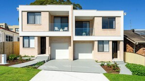 Une maison moderne à deux étages, dotée d’un garage, d’un balcon avec mobilier d’extérieur et d’un jardin bien entretenu.