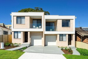 Ein modernes, zweigeschossiges Haus mit Garage, Balkon und Gartenmöbeln sowie ein gepflegter Garten.