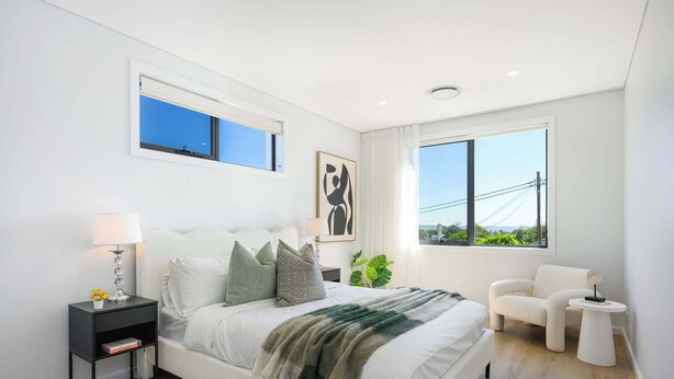 Une chambre à coucher moderne avec un grand lit, des tables de chevet, un fauteuil et une vue sur l’extérieur.
