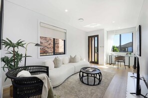 Ein modernes Wohnzimmer mit einem weißen Sofa, einem schwarzen Rattanstuhl, einem runden Couchtisch und einer Wand mit Ziegeloptik.