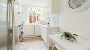 Cucina con mobili bianchi, una finestra vista alberi, lavello e fornello.