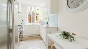 A kitchen with white cabinets, a window with a view of trees, a sink, and a stove. - The Rockley Sunlit Urban Apartment (South Yarra)