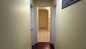 Een hal met een houten vloer, beige wanden en een deur aan het einde die leidt naar een kamer met betegelde vloer.