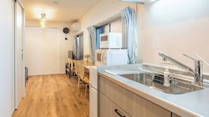 A modern kitchen with wooden cabinets, a stainless steel sink, and a dining area with chairs. - Haneda kodate HT3 (Ota)