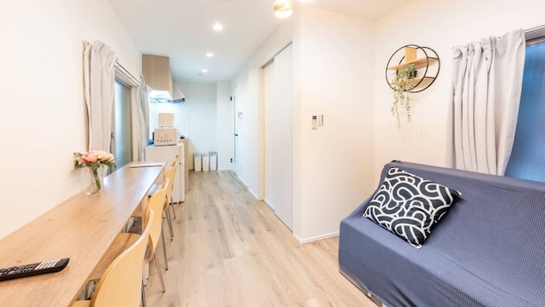 A modern room with a sofa, a dining table with chairs, a remote control, and a vase with flowers. - Haneda kodate HT3 (Ota)