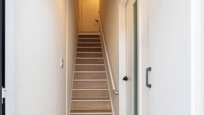 A narrow hallway with a wooden staircase, a door with a green frame, and a pair of shoes on the floor. - Haneda kodate HT3 (Ota)