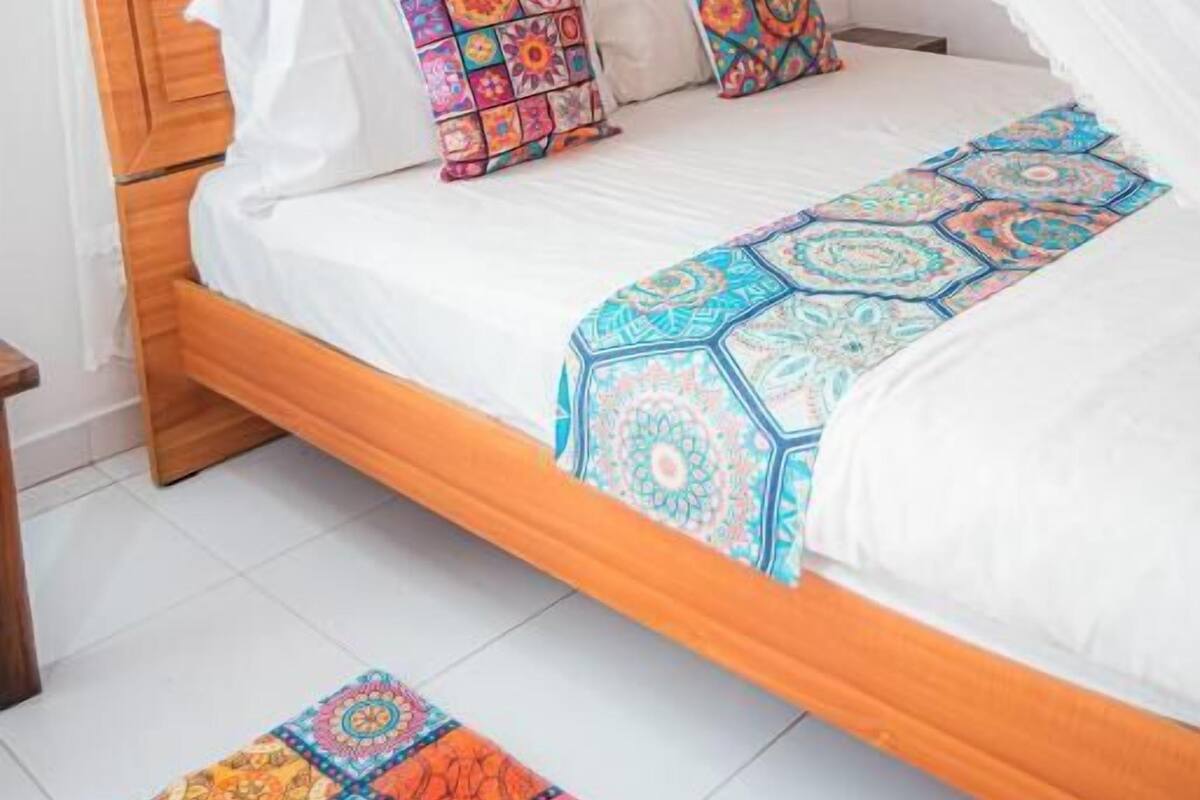 Un lit avec une tête de lit en bois, une literie blanche, des coussins colorés et un baldaquin.