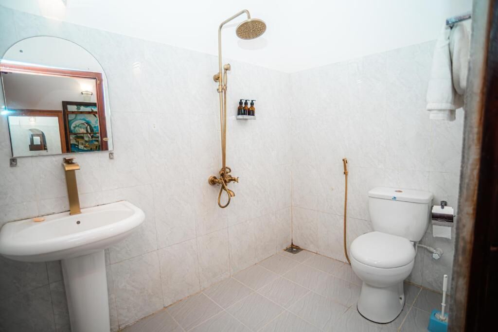 A bathroom with a pedestal sink, a toilet, a shower with a handheld showerhead, and a mirror with a decorative frame.