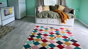 Una habitación con una cama, un armario blanco, un refrigerador blanco y una estufa blanca, además de una alfombra colorida.
