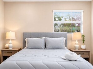 Quarto com uma cama, duas mesas de cabeceira com luminárias, uma janela com persianas e uma planta sobre uma das mesas.