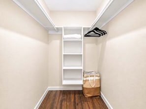 Ein begehbarer Kleiderschrank mit weißen Regalen, einer Kleiderstange und einer braunen Tasche auf dem Boden.
