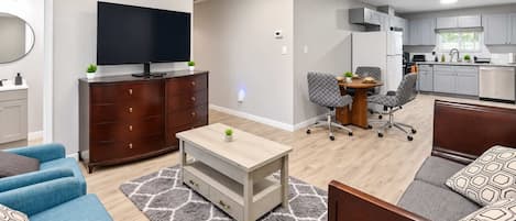 Een moderne woonkamer met een televisie, bank, salontafel en een keuken in de achtergrond.